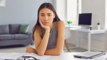 A woman looking glum at a desk with her head in her hand suggesting poor employee engagement.